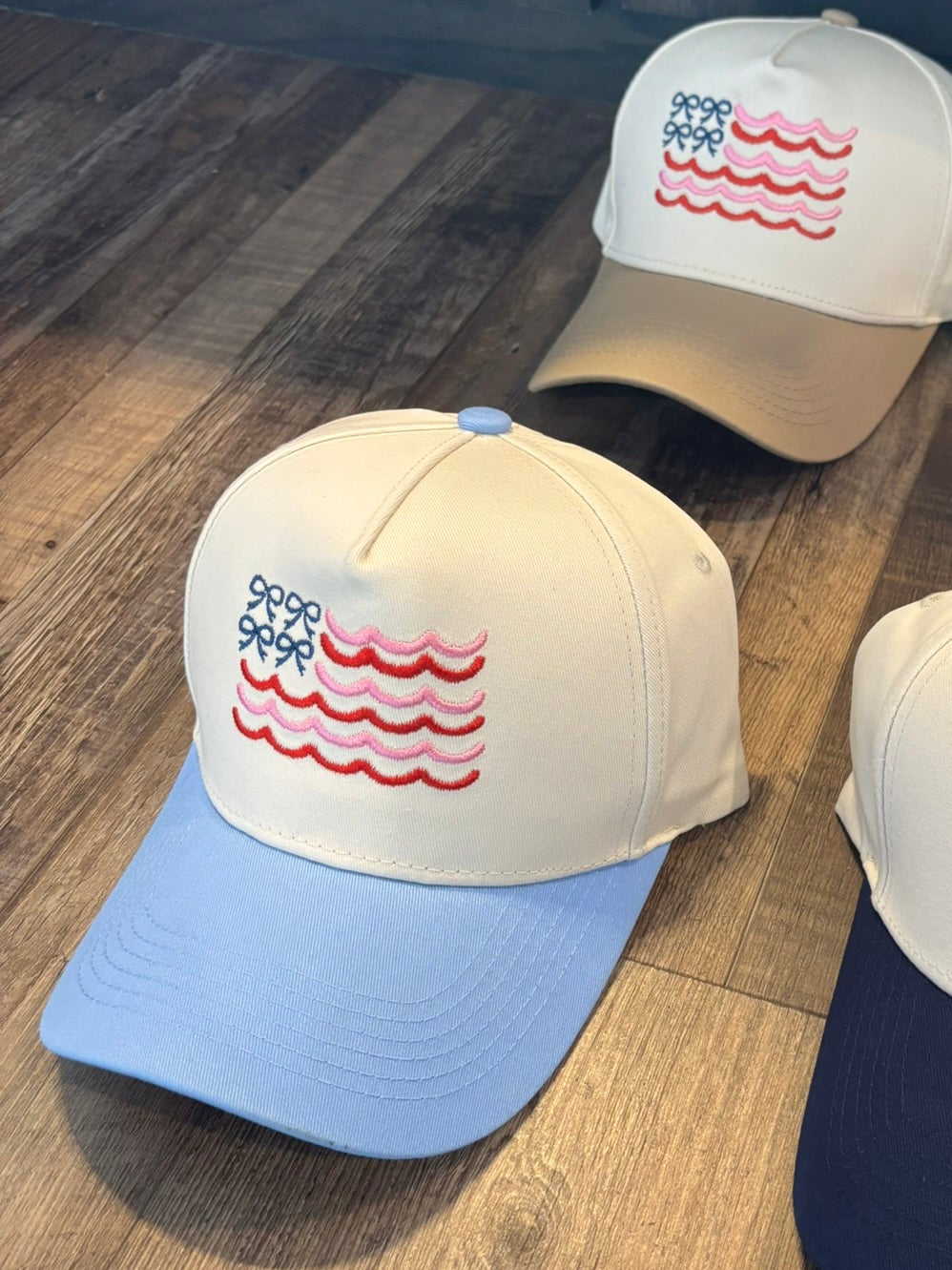 Four baseball caps with a flag design on a wooden surface.